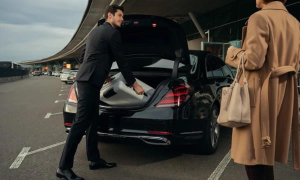 Chauffeur putting the luggage of a female client in a luxury black sedan at airport