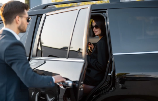 Chauffeur opening door for the lady sitting in the luxury black SUV