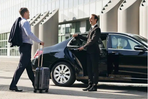 A professional chauffeur in black suit opening the door of a luxury black sedan for a male client
