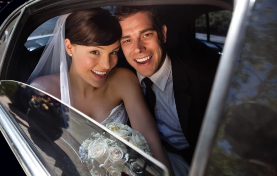 Bride and Groom smiling out from the window of a stretch limo